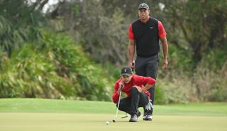 Charlie Woods lines up a putt whilst Tiger Woods looks on