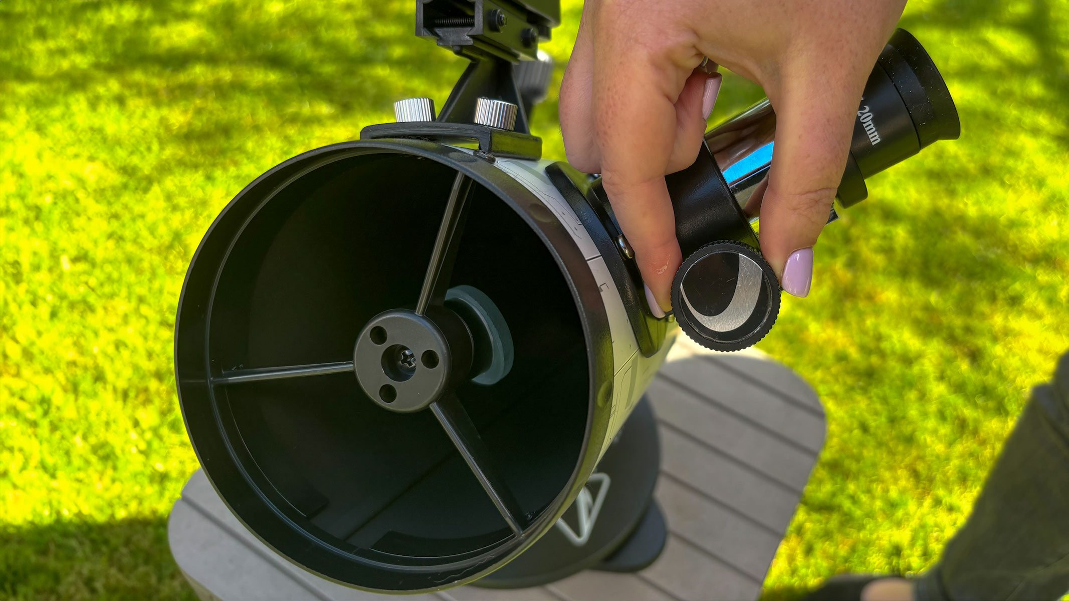 Celestron Moon Mission 100mm tabletop Dobsonian review 5 MyCelestialApp Fingers adjusting the eyepiece on the Celestron Moon Mission 100mm Tabletop Dobsonian with grass in the background.