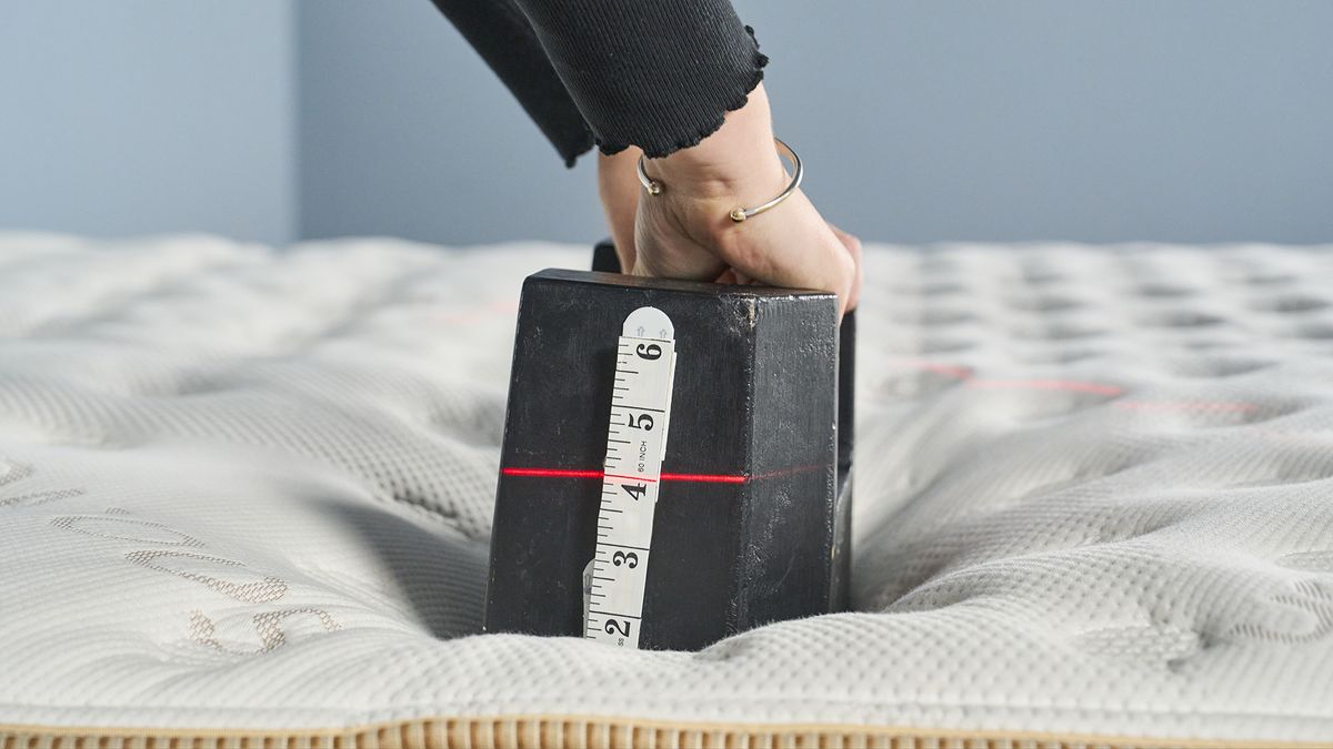 This image taken during our edge support test on the Saatva Classic shows one of our mattress testers placing a 25kg cast iron weight three inches in from the edge of the Saatva. The weight hardly sinks, showing the robust edge support of the Saatva Classic.