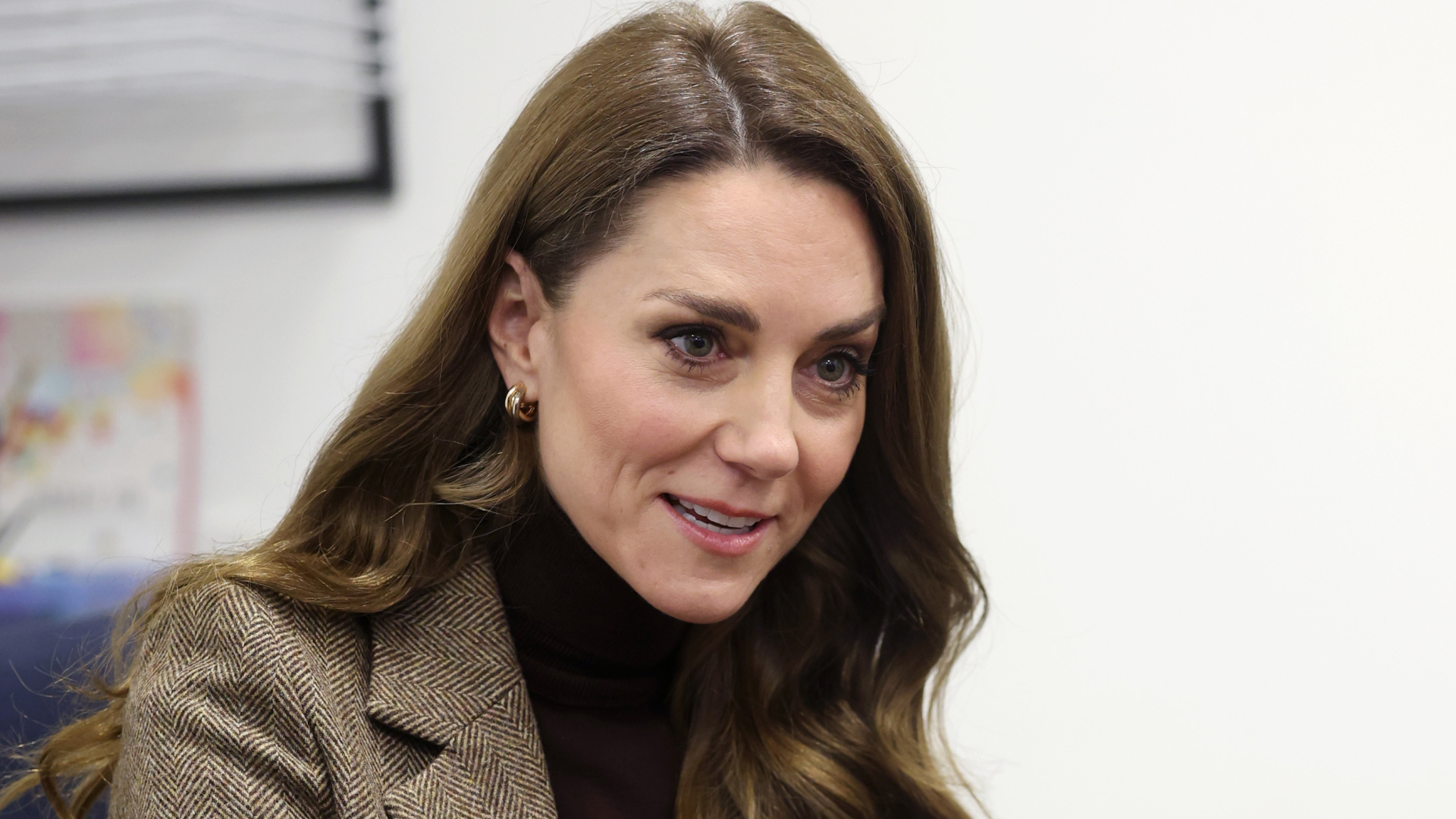 Kate Middleton wearing a tweed jacket and with long brown brunette hair with waves