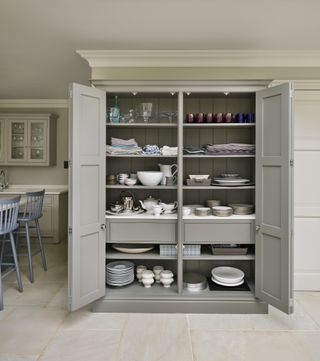 Floor to ceiling kitchen cabinet in neutral color with doors open to show shelves and drawers