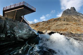 View of an elevated viewing platform that sits above the Stigfossen waterfall. A mountain can also be seen under a blue cloudy sky