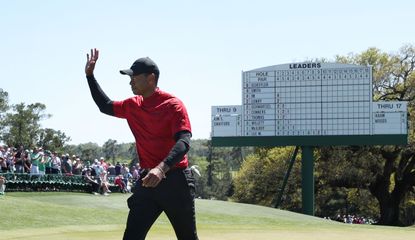 Tiger Woods waves to the crowds in front of a Masters leaderboard