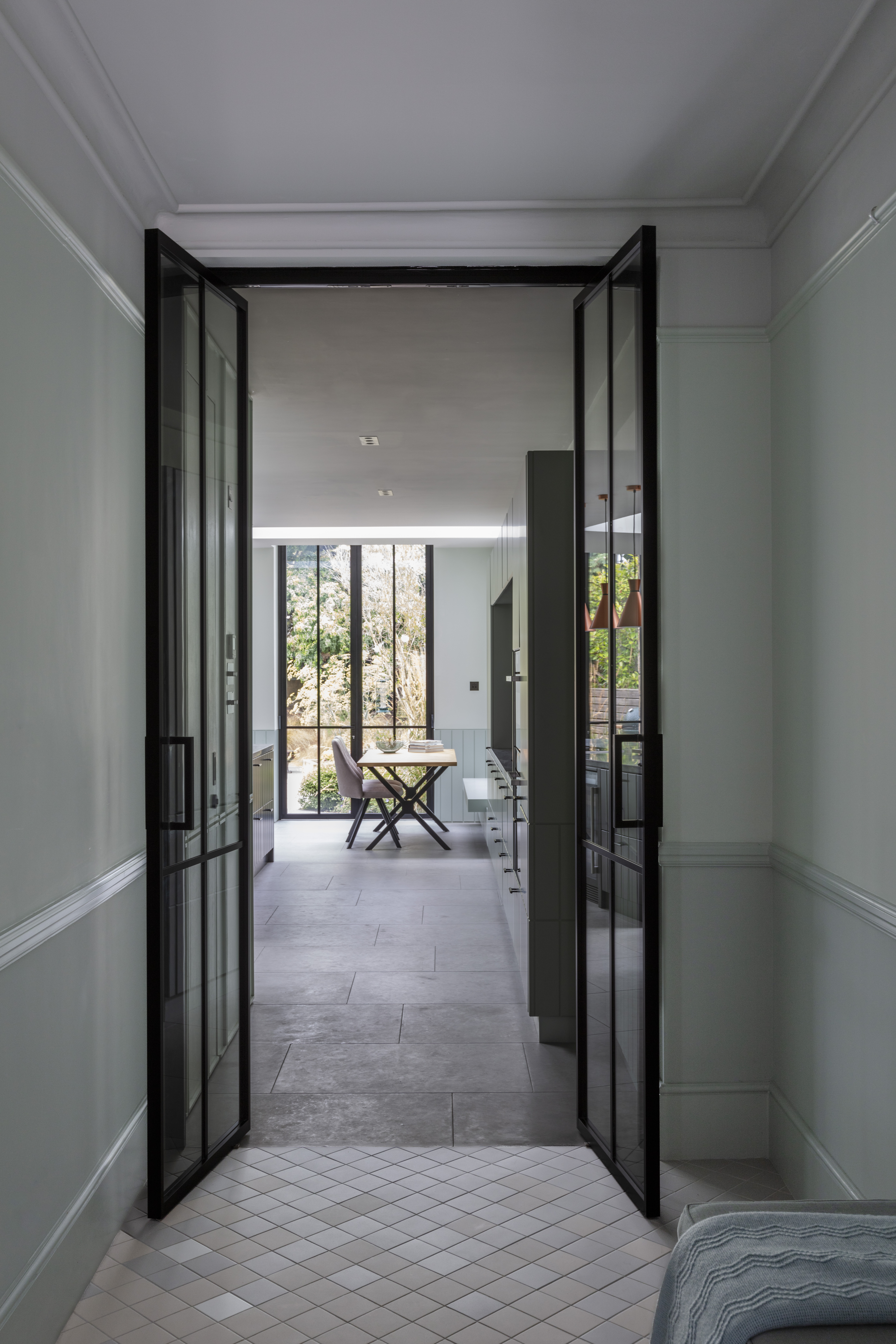 A hallway leading to the kitchen, with glass doors, and stone flooring