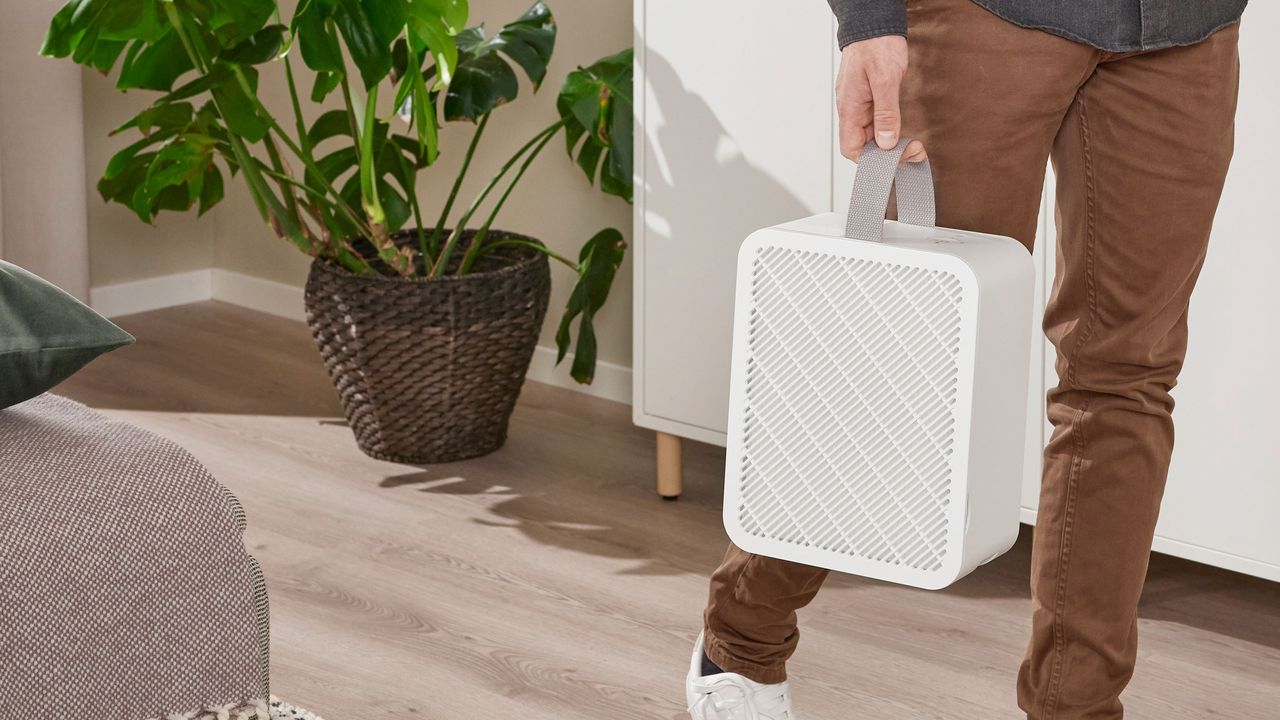 a man holding the Ikea UPPÅTVIND air purifier by the handle to move it from one room to another