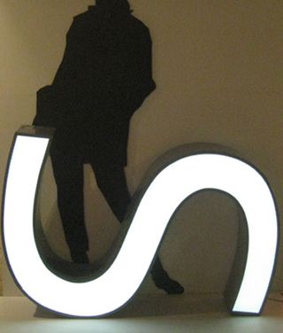 Letter "S" lit in white, on it's side in front of a silhouette of a woman