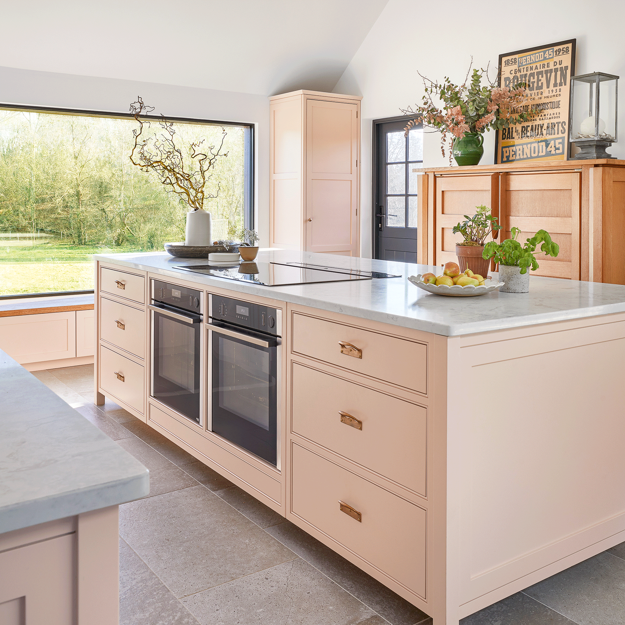 Pink kitchen with plaster pink walls, marble worktop and large kitchen islant infront of a wooden dresser.