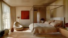 Image of a warm beige color-drenched bedroom. The canopy bed frame is chrome and there is a chrome floor lamp in the room as well.
