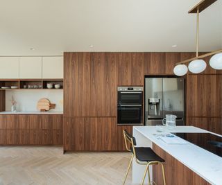 A dark wood kitchen with white countertops and white and gold modern pendant lights above the island