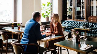 Man and woman sitting opposite each other over dinner in restaurant with glass of wine each