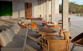 Patio area with concrete columns, wicker charis and wooden padded sofas with cushions