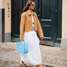 Woman wears white dress, brown jacket, jelly, and sandals. 