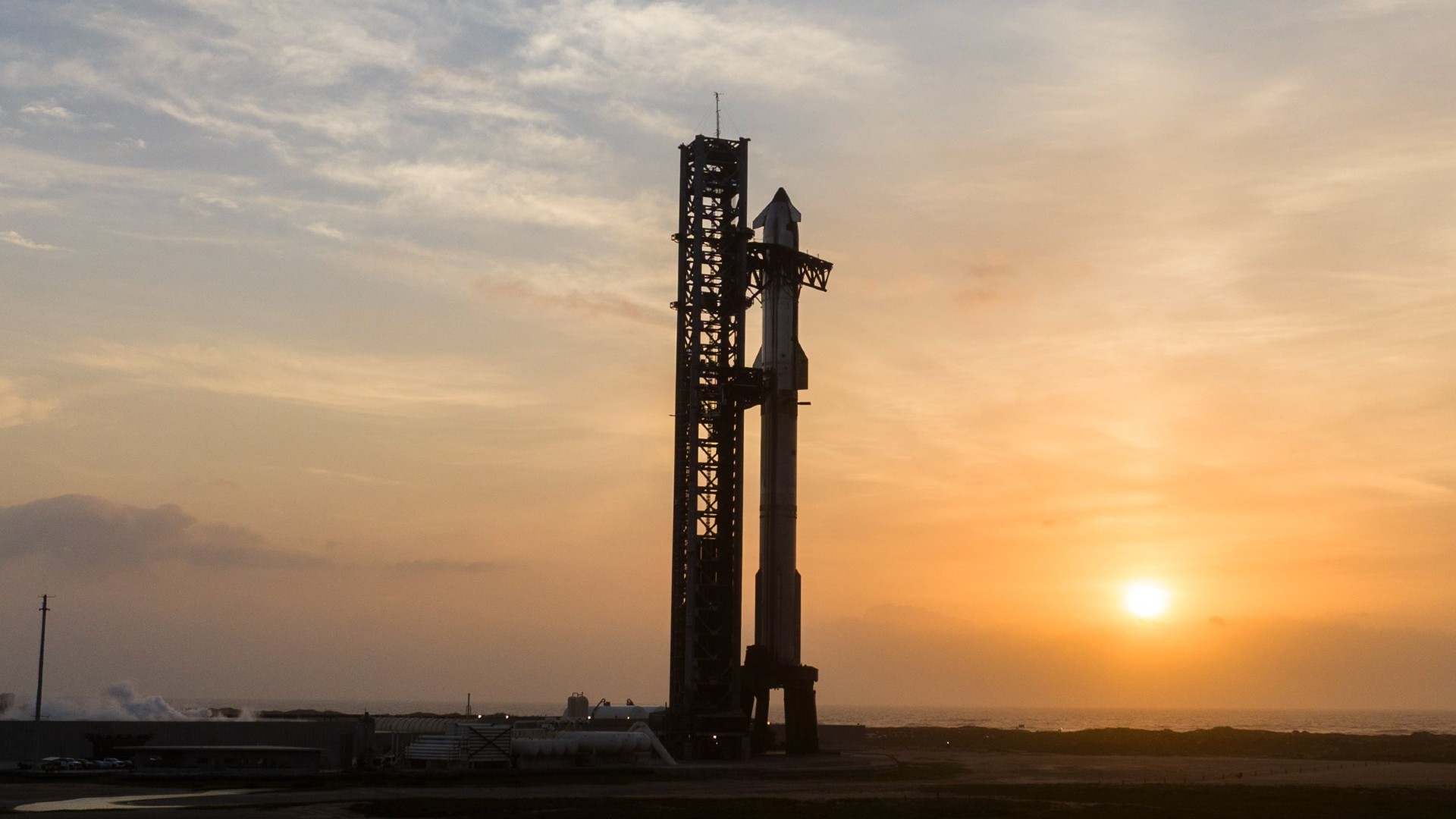 the sun rises behind a large silver rocket standing upright next to a beach