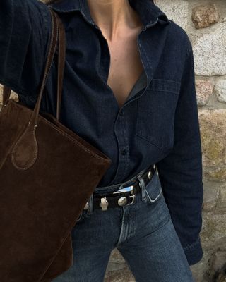 Woman wears denim shirt, denim jeans and brown suede bag