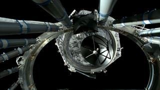 a hexagonal spacecraft floats away from a large metal ring on a black background