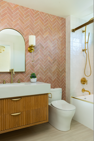 Bathroom vanity wall with terracotta colored tiles stacked in a herringbone pattern. Wooden vanity and shower with white tiles.