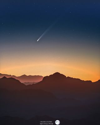 A comet with a long white tail streaks over rocky mountain landscape in the early morning sky.