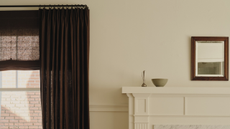 Minimalist living room featuring a mantel topped with decorative objects, a rectangular wall mirror, and a set of brown drapes.