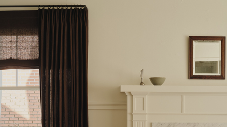 Minimalist living room featuring a mantel topped with decorative objects, a rectangular wall mirror, and a set of brown drapes.