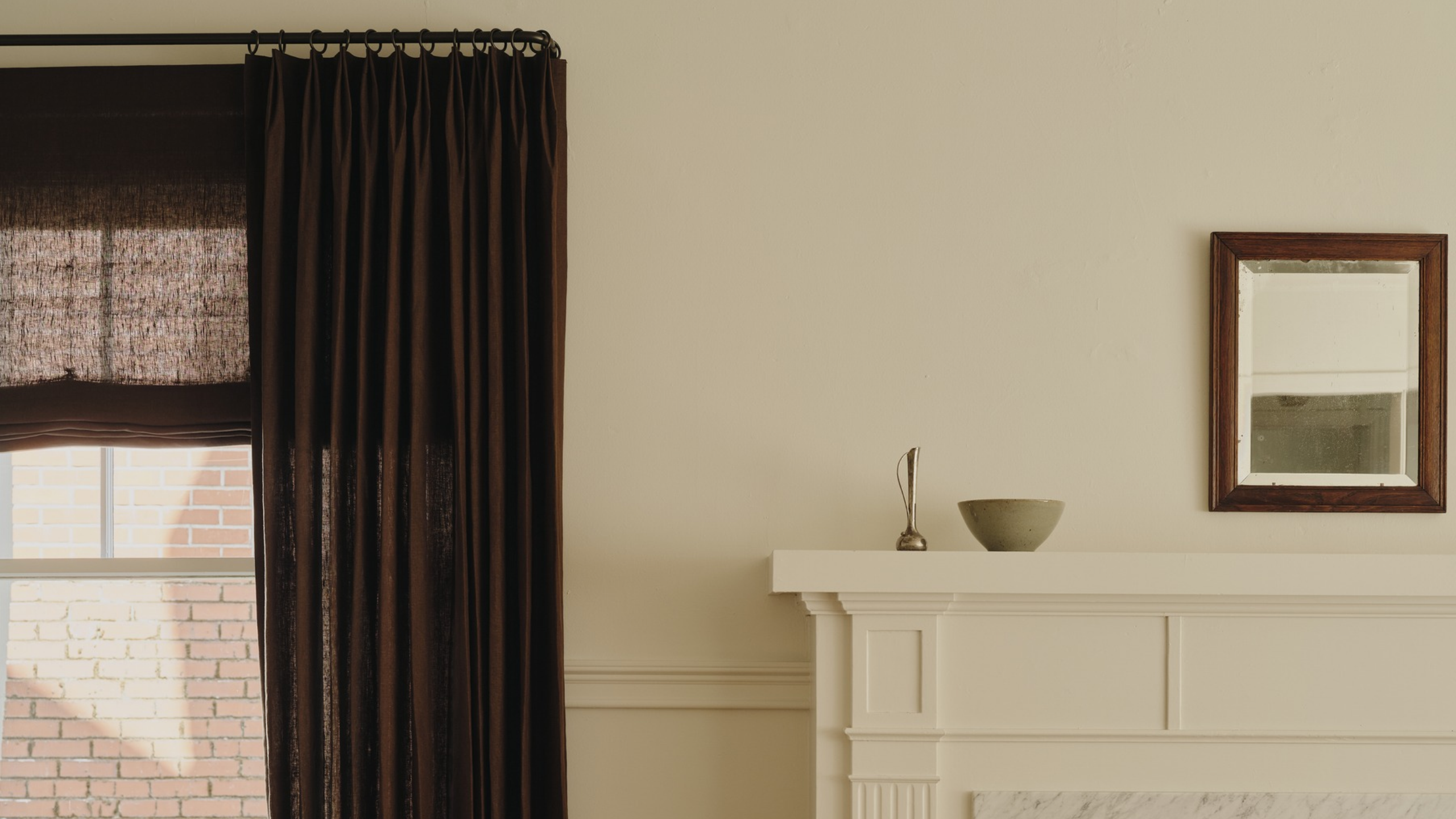 Minimalist living room featuring a mantel topped with decorative objects, a rectangular wall mirror, and a set of brown drapes.