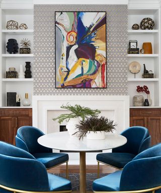 round white breakfast table with blue chairs and patterned wallpaper on chimney breast and bold artwork
