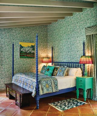 A colorful bedroom with tiled floors, floral wallpaper, a blue bedframe and a raftered ceiling