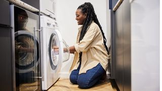Woman bending down on the floor to use a tumble dryer or washing machine.