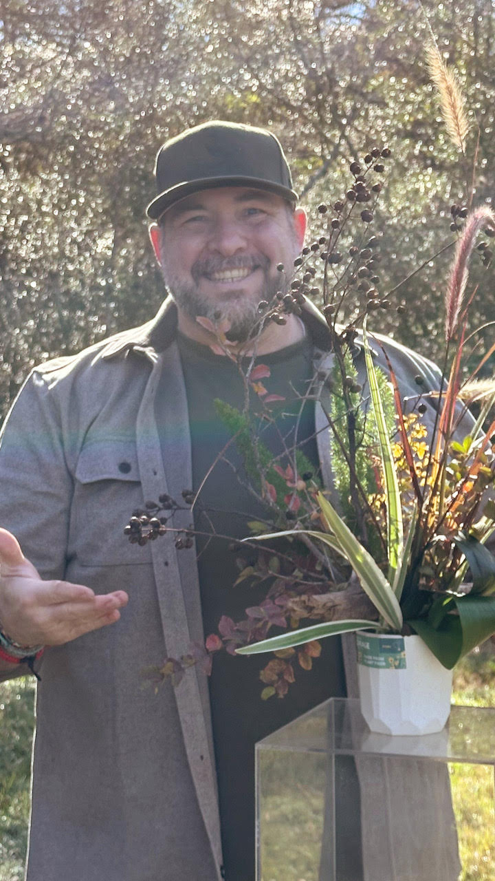 Headshot of man wearing black cap holding a foliage arrangement