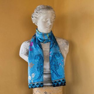 The marble bust of a woman is adorned with a brightly decorated, mosaic-filled scarf in silk against an orange background.