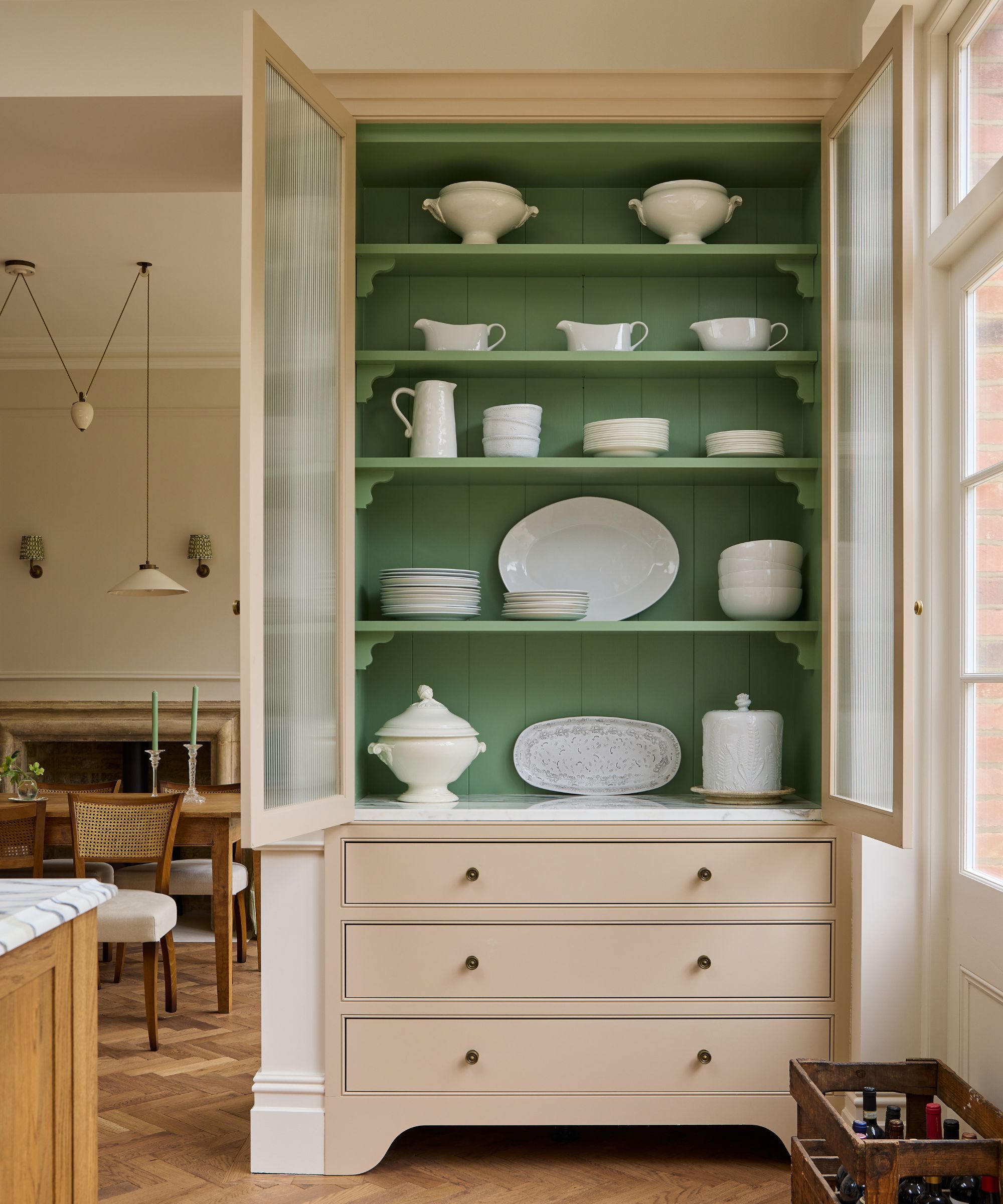 Kitchen with a built-in dresser painted cream and green, filled with white platters, gravy boats, and bowls.