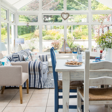 Glass panelled conservatory, rustic dining table and chairs, blue striped sofa, coastal accessories.