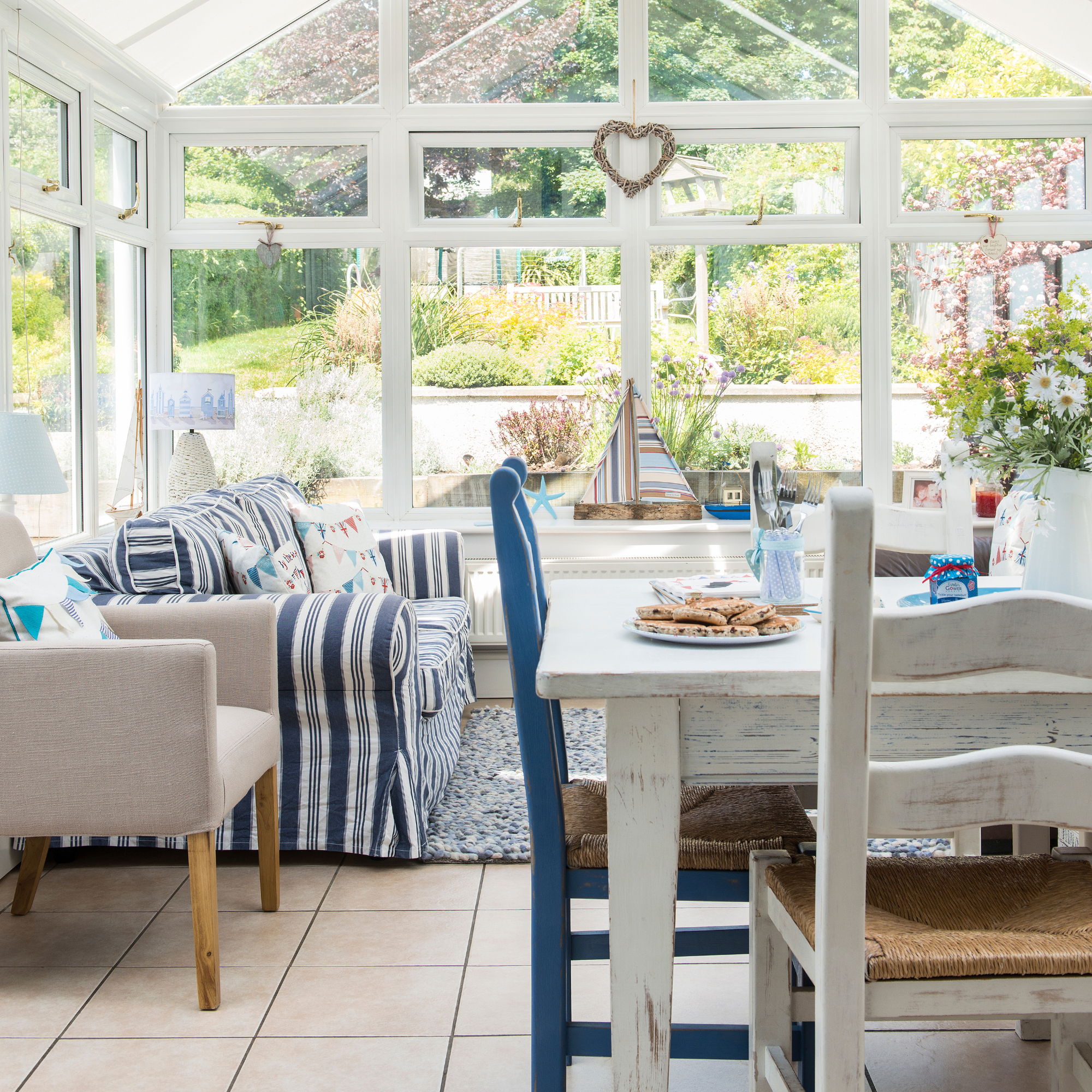 Glass panelled conservatory, rustic dining table and chairs, blue striped sofa, coastal accessories.