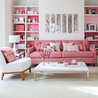 A white living room with a pink sofa and built in wall storage with a pink background