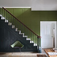 Hallway with rich green painted wall next to the stairs and navy painted panelling with wood floors