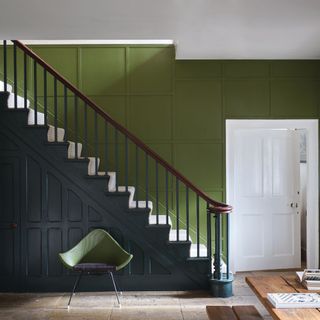 Hallway with rich green painted wall next to the stairs and navy painted panelling with stone floors