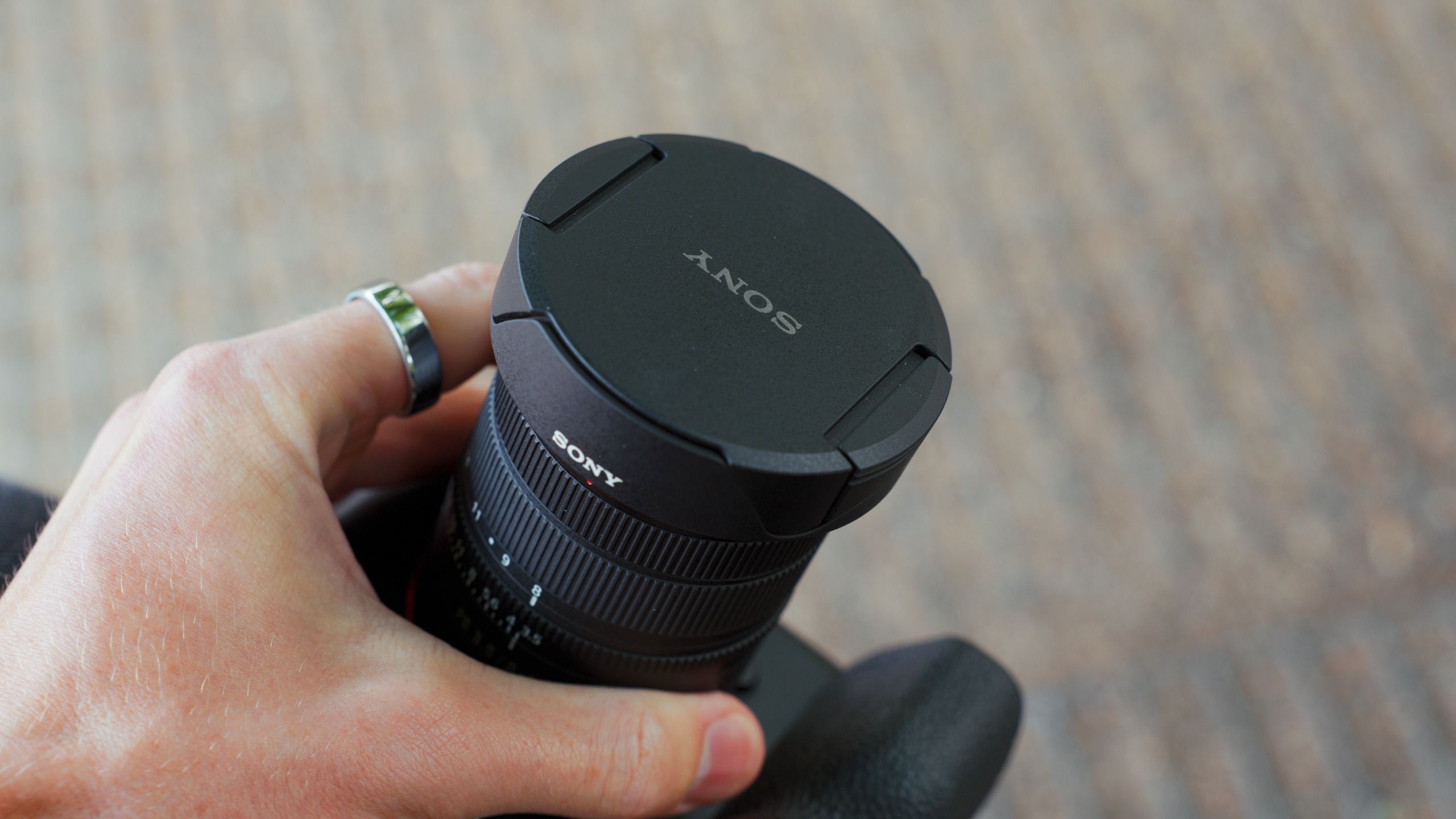 Hand holding a Sony camera fitted with the FE 8-14mm F3.5 G lens, shown with its front lens cap attached.