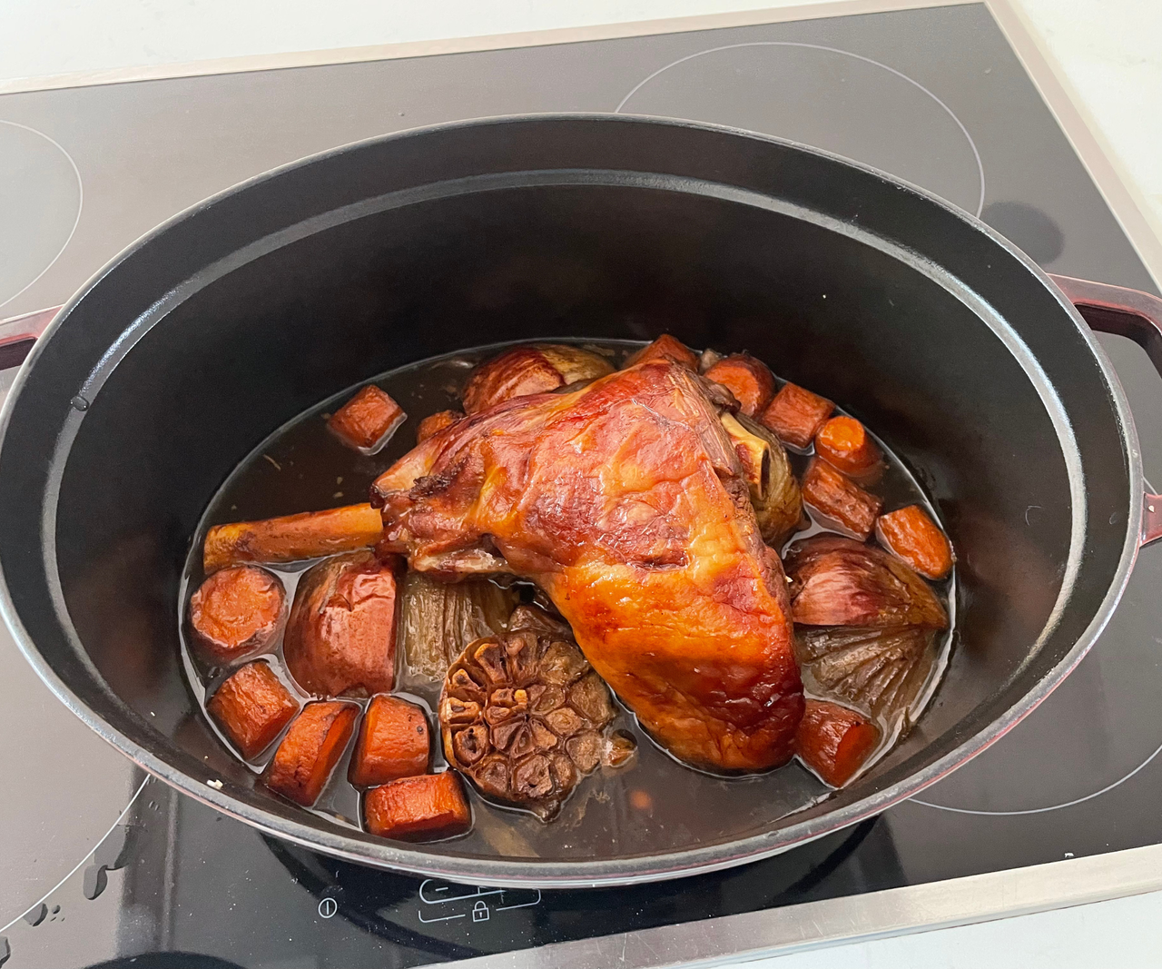 A roasted leg of lamb with vegetables inside a Dutch oven.