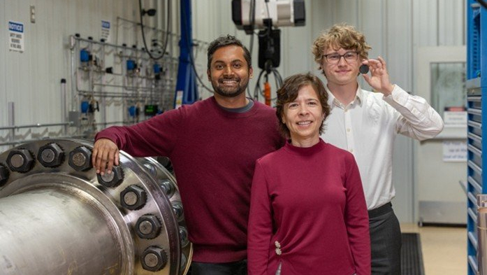 two men and a woman stand inside a scientific laboratory