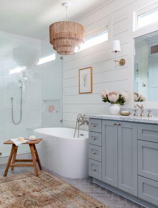 Bathroom with grey vanity, freestanding bathtub and shower, stool, and chandelier