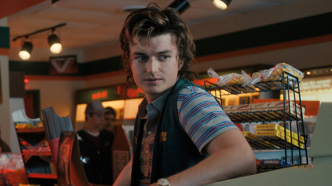 Joe Keery en la temporada 4 de Stranger Things apoyado contra una caja registradora.