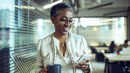 Close up of a senior businesswoman using a phone while having coffee in the office