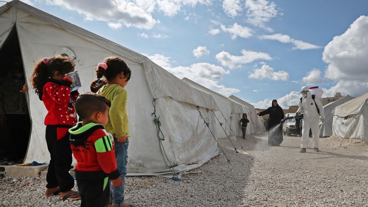 Displaced children watch as a health worker sprays disinfectant in Idlib, Syria