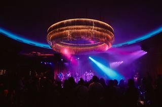 The giant circular chandelier at The Pinky Ring in Las Vegas is illuminated by red and purple strobelights in front of Bruno Mars on stage