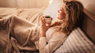 Woman drinking a cup of tea in bed and smiling to herself