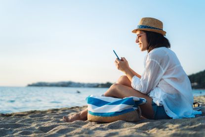 Data roaming charges: a holidaymaker sits on a beach while using her phone