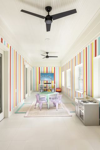 playroom with candy stripe style walls, white floor tiles, pastel chair and table, two rugs, kitchen play area, toys, shiplap ceiling