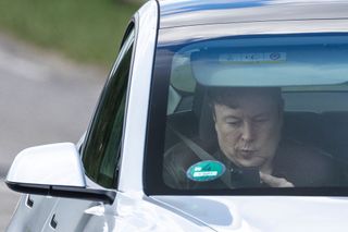 Elon Musk looks at his phone while riding in a Tesla.