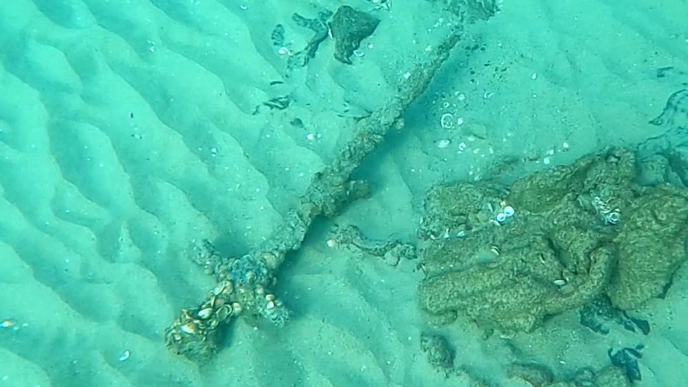 A medieval sword coated in shells at the bottom of the sea. 