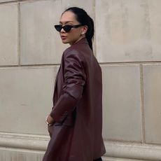 Woman wearing oxblood red suit, standing in front of wall taking outfit picture.