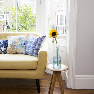 living room with flower on vase and sofa with cushions and glass window